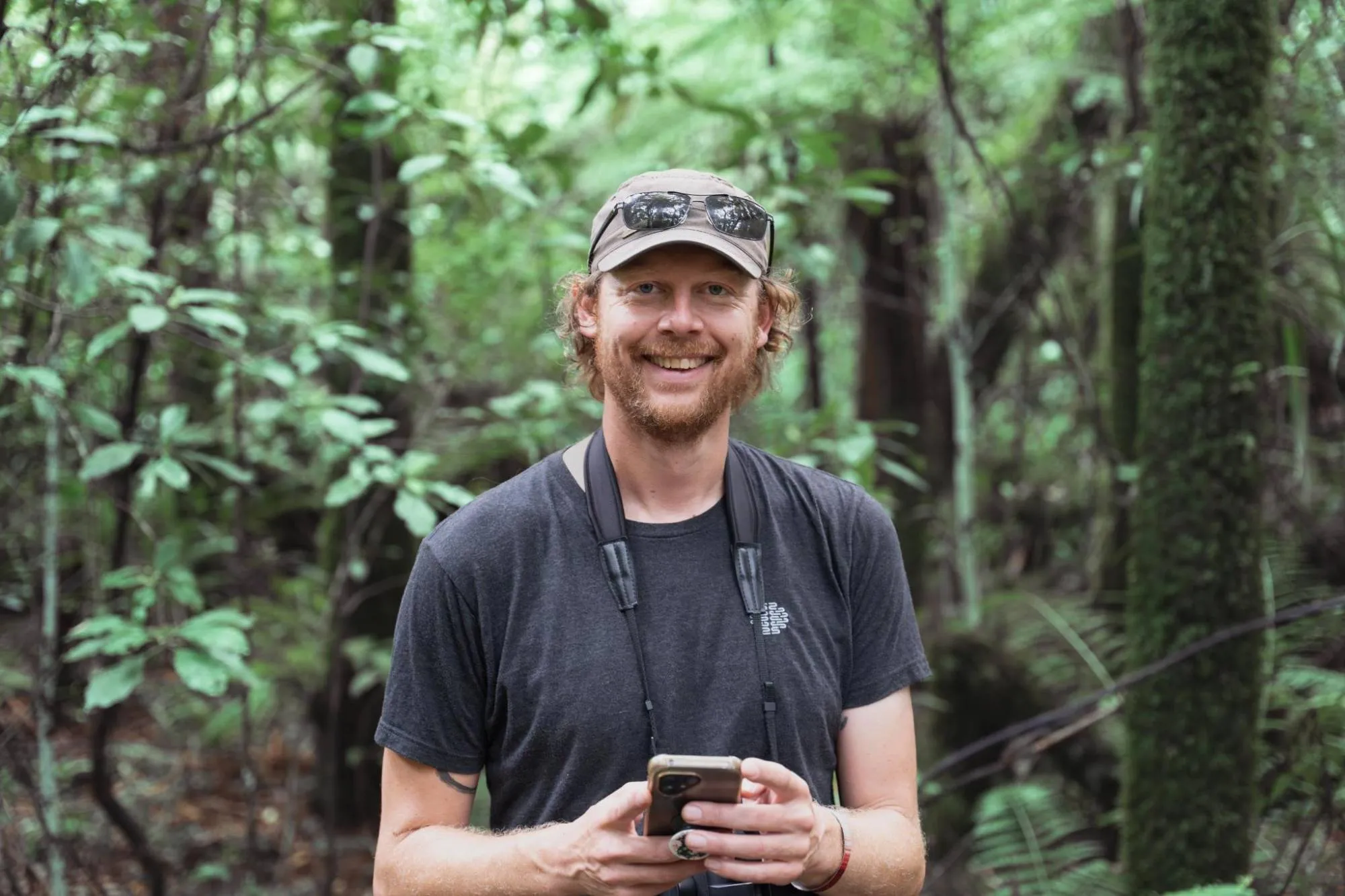 Stephan in het bos, met een verrekijker om en een telefoon in zijn handen